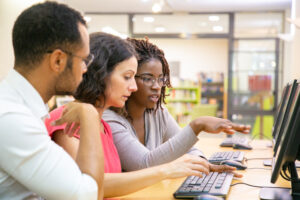 Three educators look at the same computer screen in a computer lab. 