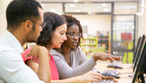 Three educators look at the same computer screen in a computer lab.