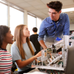 Teacher with Two College Students Building Machine In Science Robotics or Engineering Class