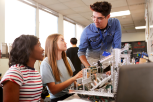 Teacher with Two College Students Building Machine In Science Robotics or Engineering Class